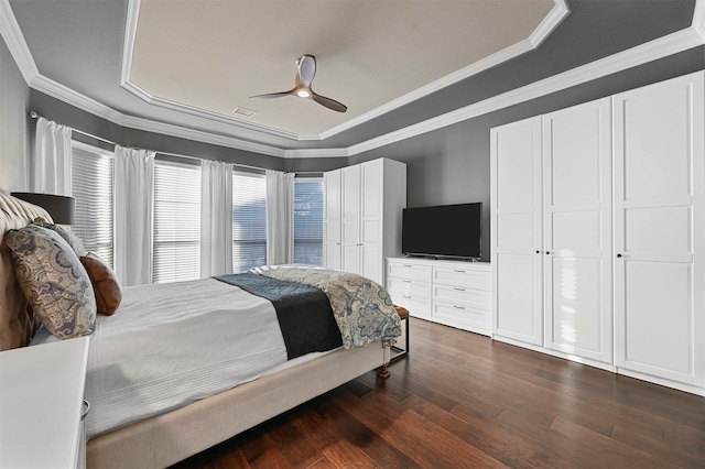 bedroom with dark wood-style floors, a tray ceiling, ornamental molding, and a ceiling fan