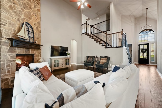 living room with arched walkways, a fireplace, stairway, hardwood / wood-style floors, and baseboards