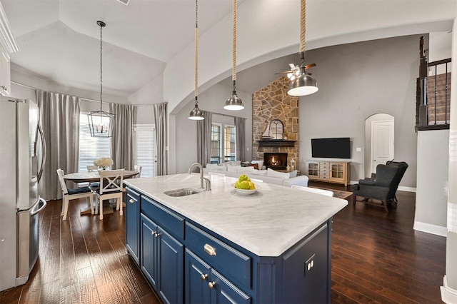 kitchen featuring arched walkways, dark wood-type flooring, blue cabinetry, stainless steel refrigerator with ice dispenser, and a sink