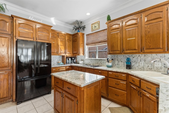 kitchen featuring sink, a center island, light tile patterned floors, black refrigerator, and ornamental molding