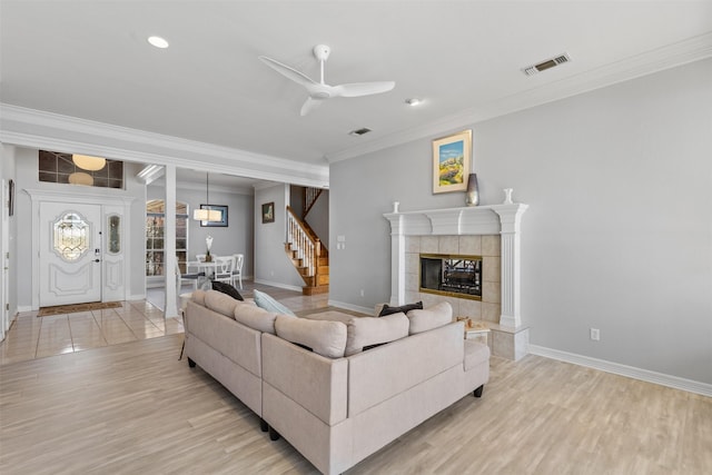 living room featuring crown molding, a tile fireplace, light hardwood / wood-style floors, and ceiling fan