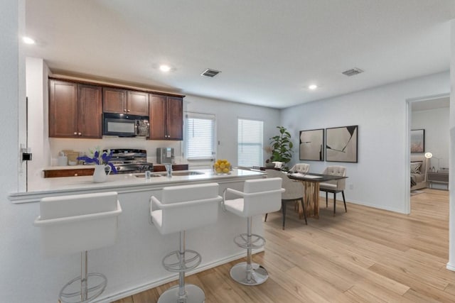 kitchen featuring sink, stainless steel stove, a kitchen bar, kitchen peninsula, and light wood-type flooring