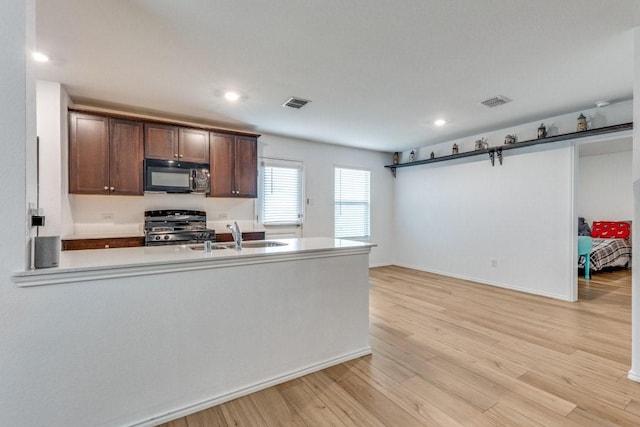 kitchen featuring dark brown cabinetry, sink, range, light wood-type flooring, and a barn door