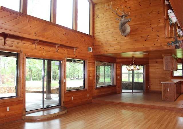 unfurnished living room featuring a towering ceiling, light hardwood / wood-style floors, and wood walls