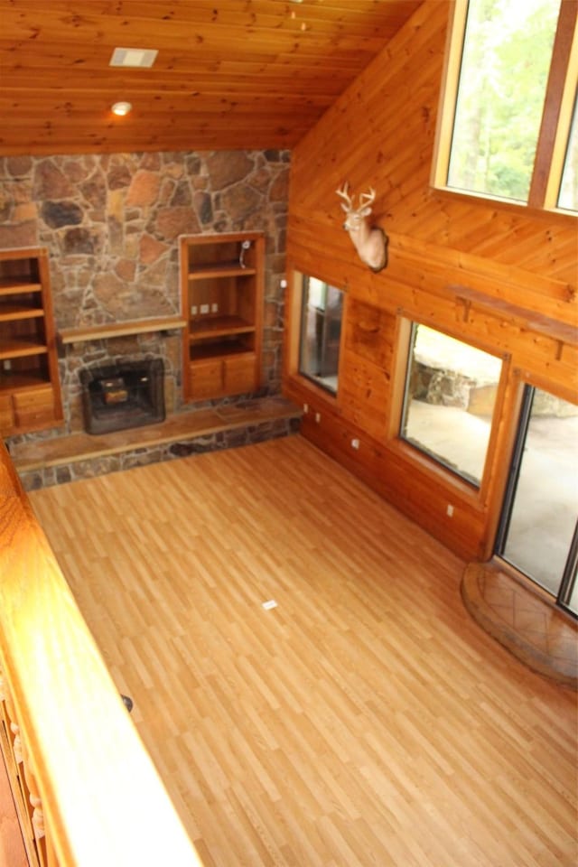 unfurnished living room with wood ceiling, wooden walls, wood-type flooring, and a stone fireplace