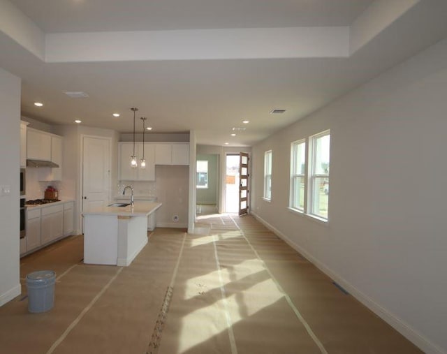 kitchen featuring white cabinetry, stainless steel gas stovetop, a kitchen island with sink, and hanging light fixtures