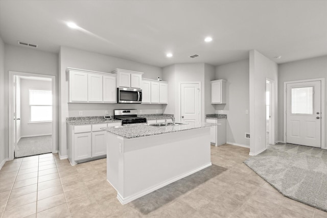 kitchen with light stone counters, stainless steel appliances, an island with sink, and white cabinets