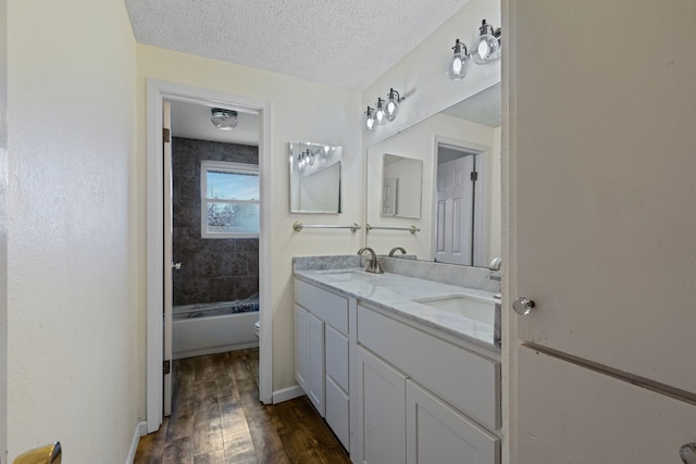 full bathroom featuring tiled shower / bath combo, vanity, wood-type flooring, a textured ceiling, and toilet