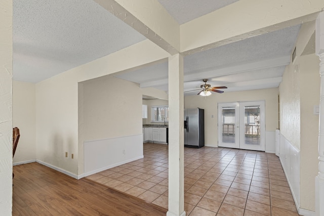 tiled empty room featuring ceiling fan, a textured ceiling, and beamed ceiling