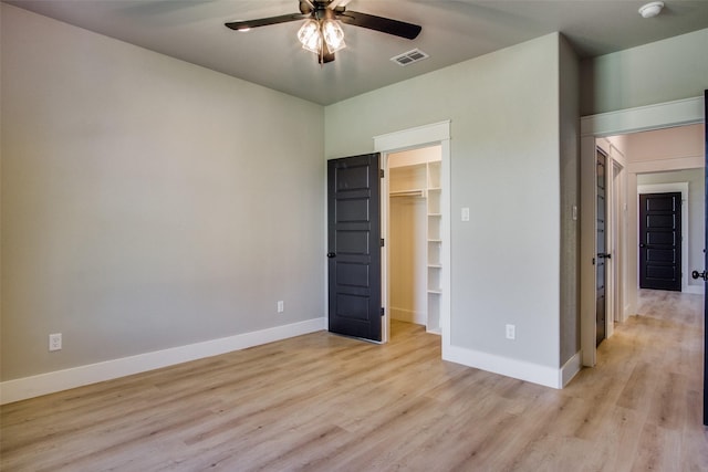 unfurnished bedroom featuring a spacious closet, light hardwood / wood-style flooring, a closet, and ceiling fan