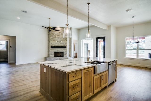 kitchen with a fireplace, decorative light fixtures, a kitchen island with sink, light hardwood / wood-style floors, and beam ceiling