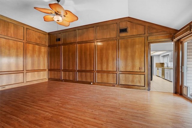 unfurnished room with wood walls, lofted ceiling, sink, ceiling fan, and light wood-type flooring