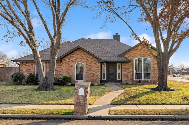 view of front of property featuring roof with shingles, a chimney, a front lawn, and brick siding