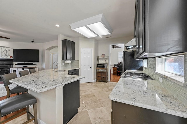 kitchen with sink, light stone counters, kitchen peninsula, ceiling fan, and range hood