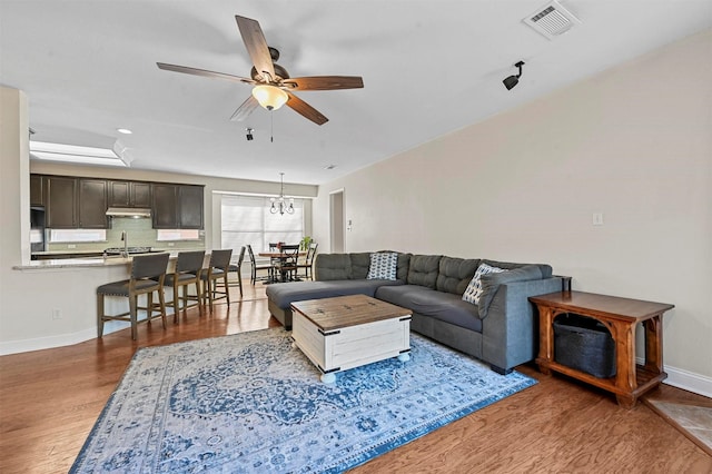 living room with ceiling fan with notable chandelier, wood-type flooring, and sink