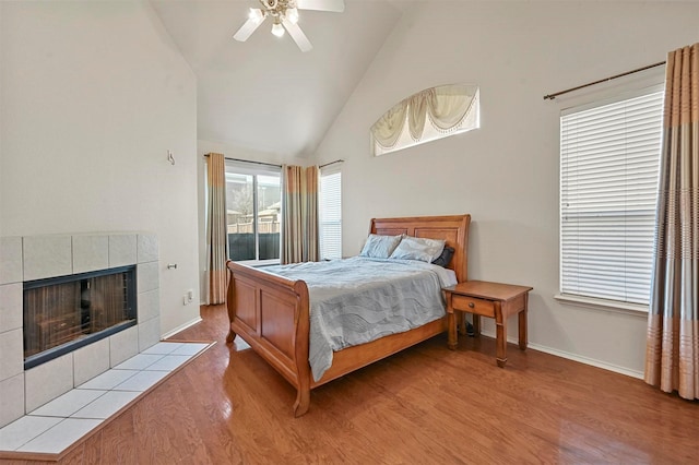 bedroom featuring ceiling fan, high vaulted ceiling, a fireplace, light hardwood / wood-style floors, and access to outside