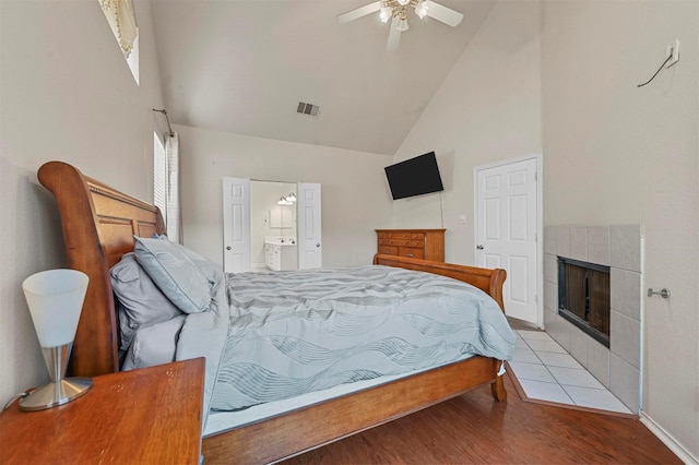 bedroom featuring ensuite bath, a tile fireplace, light hardwood / wood-style floors, ceiling fan, and high vaulted ceiling