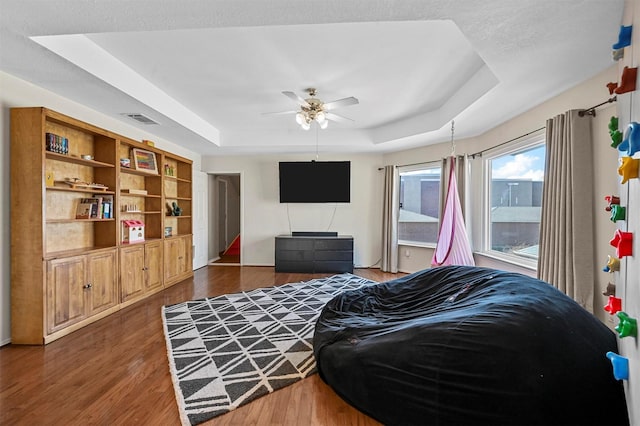 living room with ceiling fan, a tray ceiling, and dark wood-type flooring