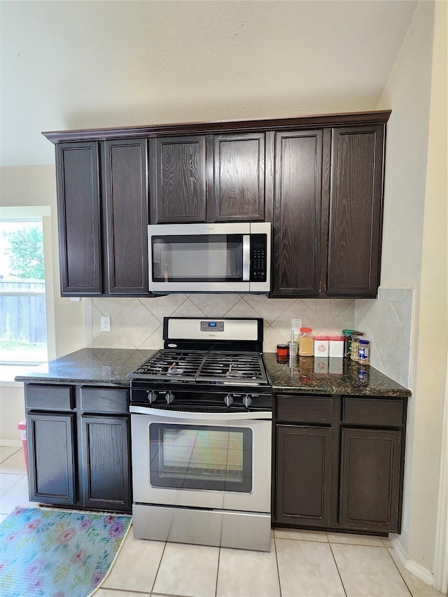 kitchen featuring dark stone countertops, backsplash, dark brown cabinets, and appliances with stainless steel finishes