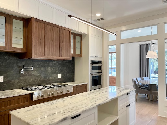 kitchen with stainless steel appliances, white cabinetry, light stone countertops, and backsplash