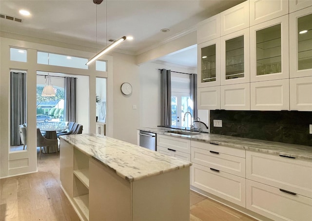 kitchen featuring decorative light fixtures, sink, white cabinets, a center island, and light stone countertops