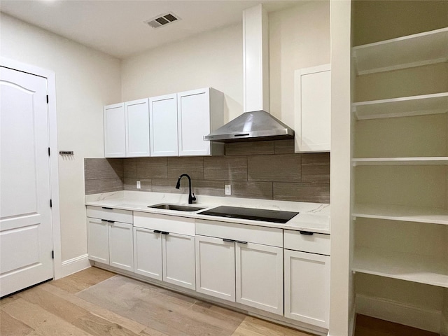 kitchen featuring black electric stovetop, sink, wall chimney range hood, and white cabinets