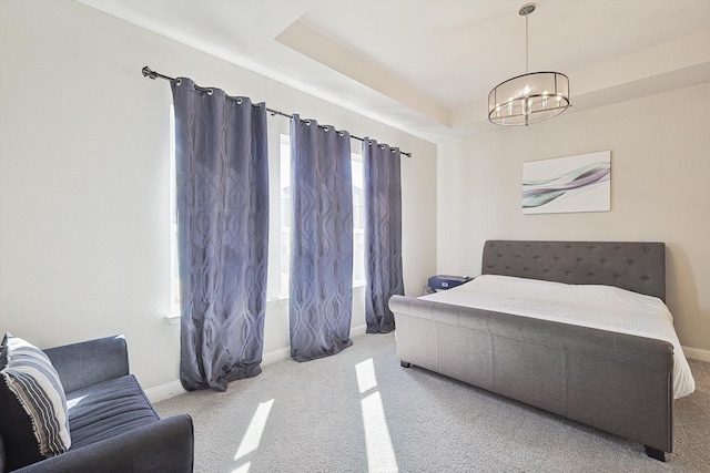 carpeted bedroom featuring a tray ceiling and a chandelier