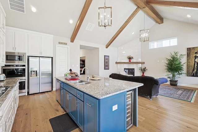 kitchen featuring an island with sink, sink, white cabinets, stainless steel appliances, and blue cabinetry