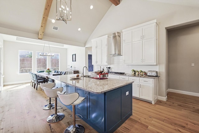 kitchen with a center island with sink, white cabinetry, pendant lighting, and wall chimney exhaust hood