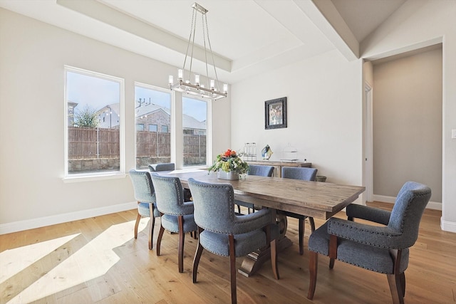 dining area with a notable chandelier, a tray ceiling, and light wood-type flooring