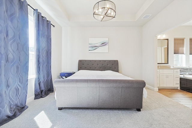 carpeted bedroom featuring connected bathroom, a raised ceiling, and a chandelier