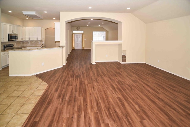 kitchen with vaulted ceiling, tasteful backsplash, white cabinetry, light hardwood / wood-style floors, and stainless steel appliances