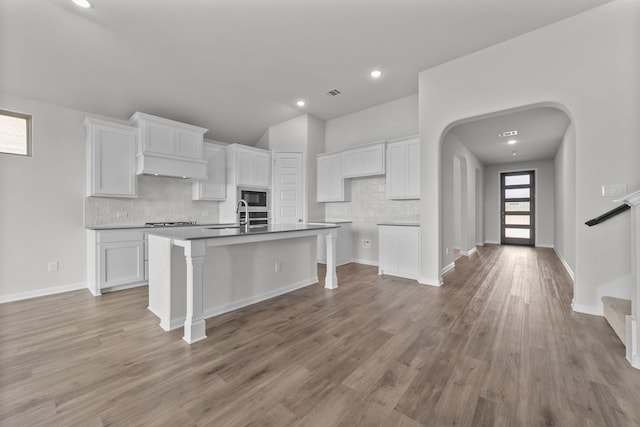 kitchen with a kitchen island with sink, built in microwave, light hardwood / wood-style floors, and white cabinets