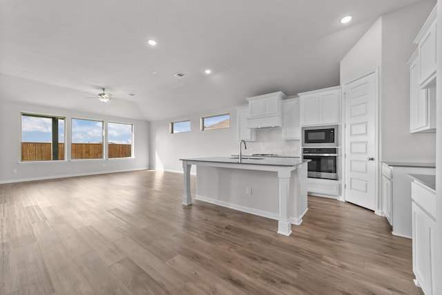 kitchen with built in microwave, sink, white cabinetry, stainless steel oven, and a center island with sink