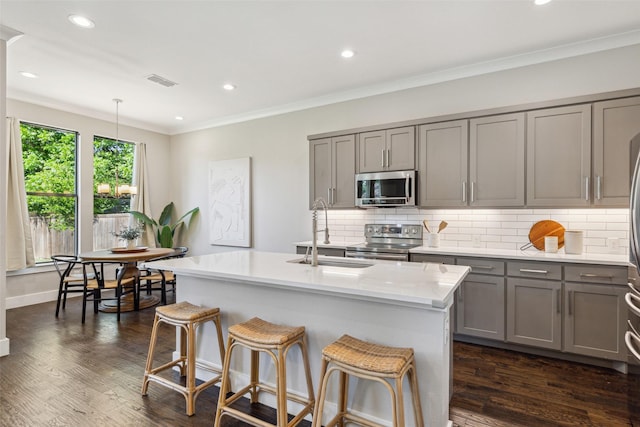 kitchen featuring appliances with stainless steel finishes, decorative light fixtures, sink, backsplash, and a kitchen island with sink