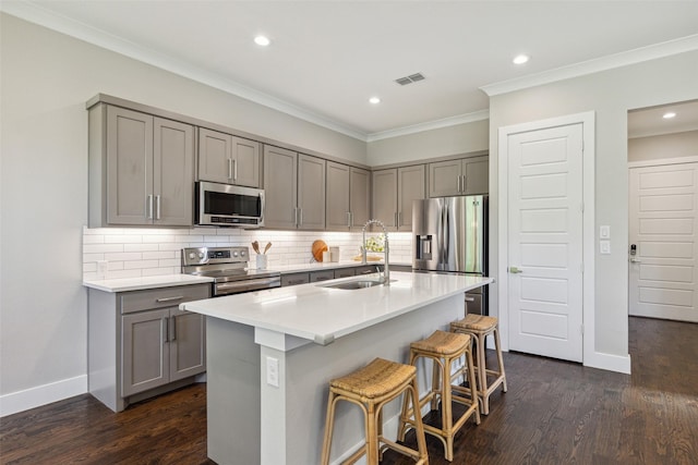 kitchen featuring dark wood-type flooring, sink, an island with sink, stainless steel appliances, and backsplash