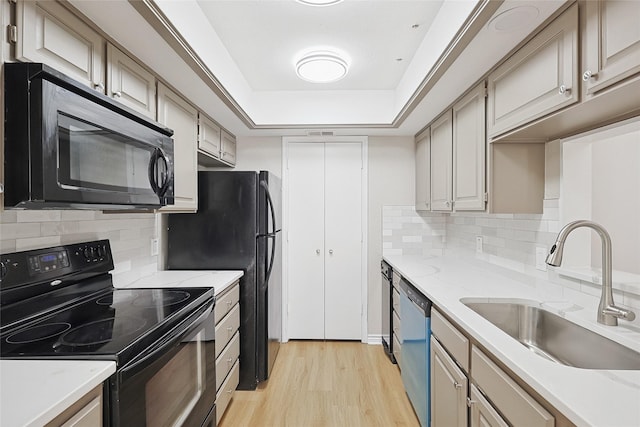 kitchen with tasteful backsplash, sink, black appliances, a raised ceiling, and light wood-type flooring