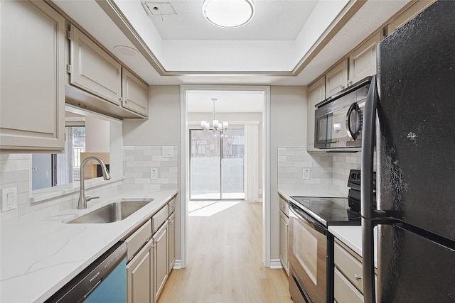 kitchen with sink, light hardwood / wood-style flooring, appliances with stainless steel finishes, a tray ceiling, and decorative light fixtures