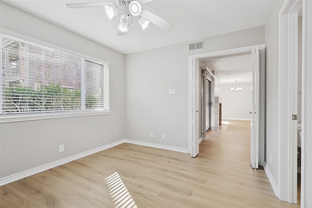 spare room with ceiling fan with notable chandelier and light wood-type flooring