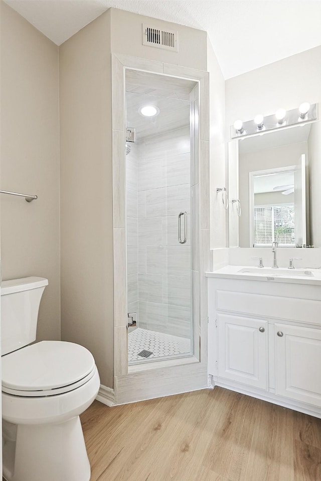 bathroom featuring wood-type flooring, toilet, a shower with door, and vanity