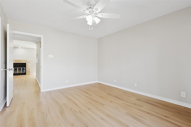 empty room with ceiling fan, a tiled fireplace, and light hardwood / wood-style flooring