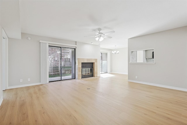 unfurnished living room with a tiled fireplace, ceiling fan with notable chandelier, and light hardwood / wood-style flooring