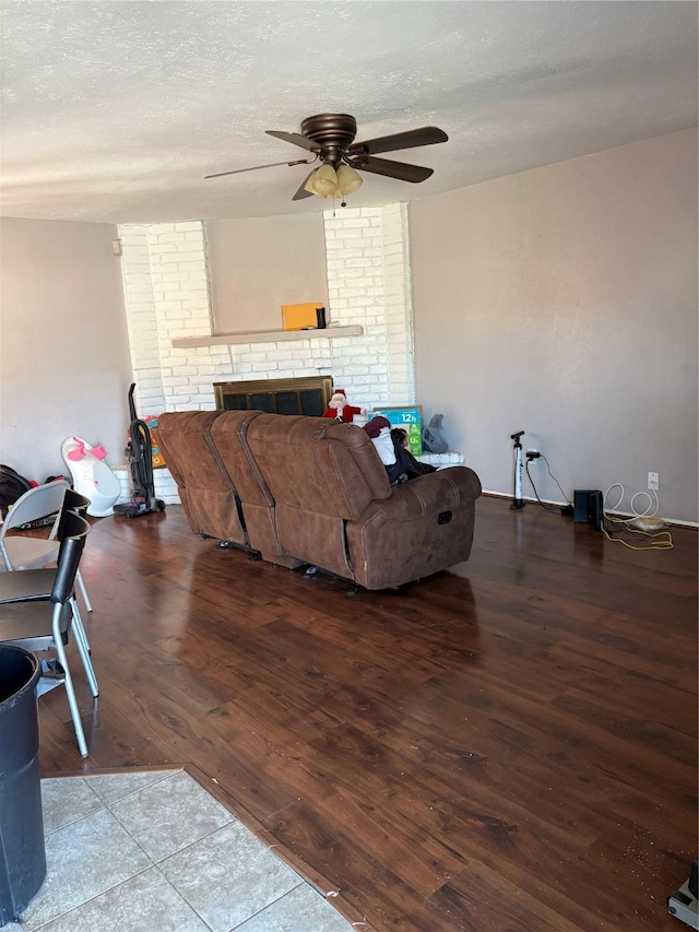 living room featuring ceiling fan, hardwood / wood-style floors, a brick fireplace, and a textured ceiling