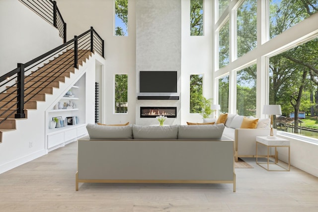 living room with built in shelves, a fireplace, light hardwood / wood-style floors, and a towering ceiling