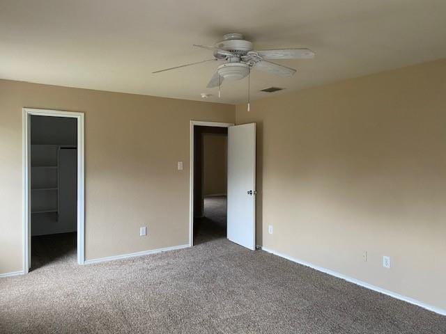 unfurnished bedroom featuring ceiling fan, a walk in closet, a closet, and carpet