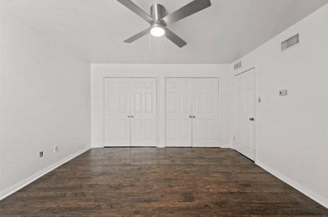 unfurnished bedroom featuring ceiling fan, two closets, and dark hardwood / wood-style flooring