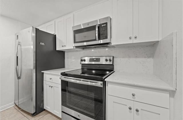 kitchen featuring white cabinetry, stainless steel appliances, light stone counters, and light tile patterned floors