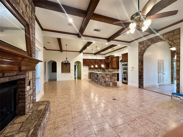 unfurnished living room featuring ceiling fan, a stone fireplace, coffered ceiling, and beam ceiling