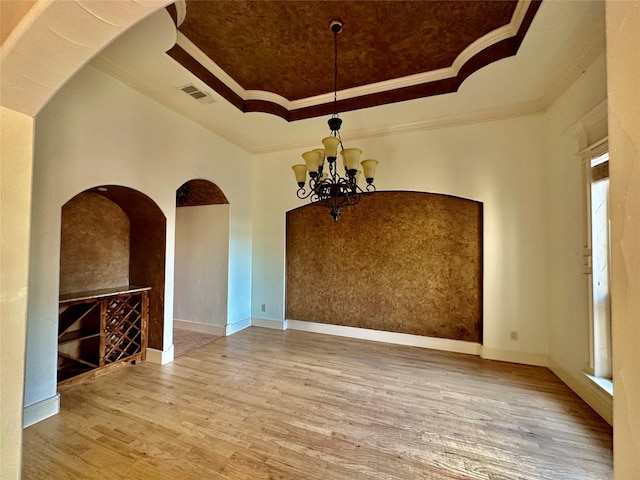 spare room featuring hardwood / wood-style flooring, ornamental molding, a raised ceiling, and a notable chandelier