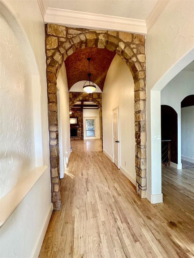 hallway with lofted ceiling, crown molding, and light wood-type flooring